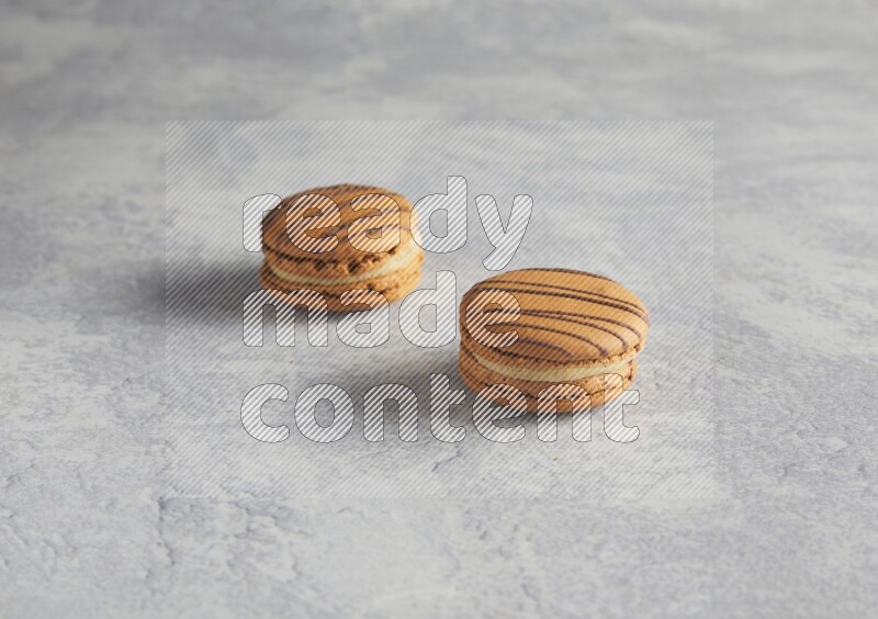 45º Shot of two light brown  Almond Cream macarons  on white  marble background