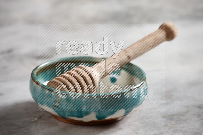Multicolored pottery bowl with wooden honey dipper in it on grey marble background