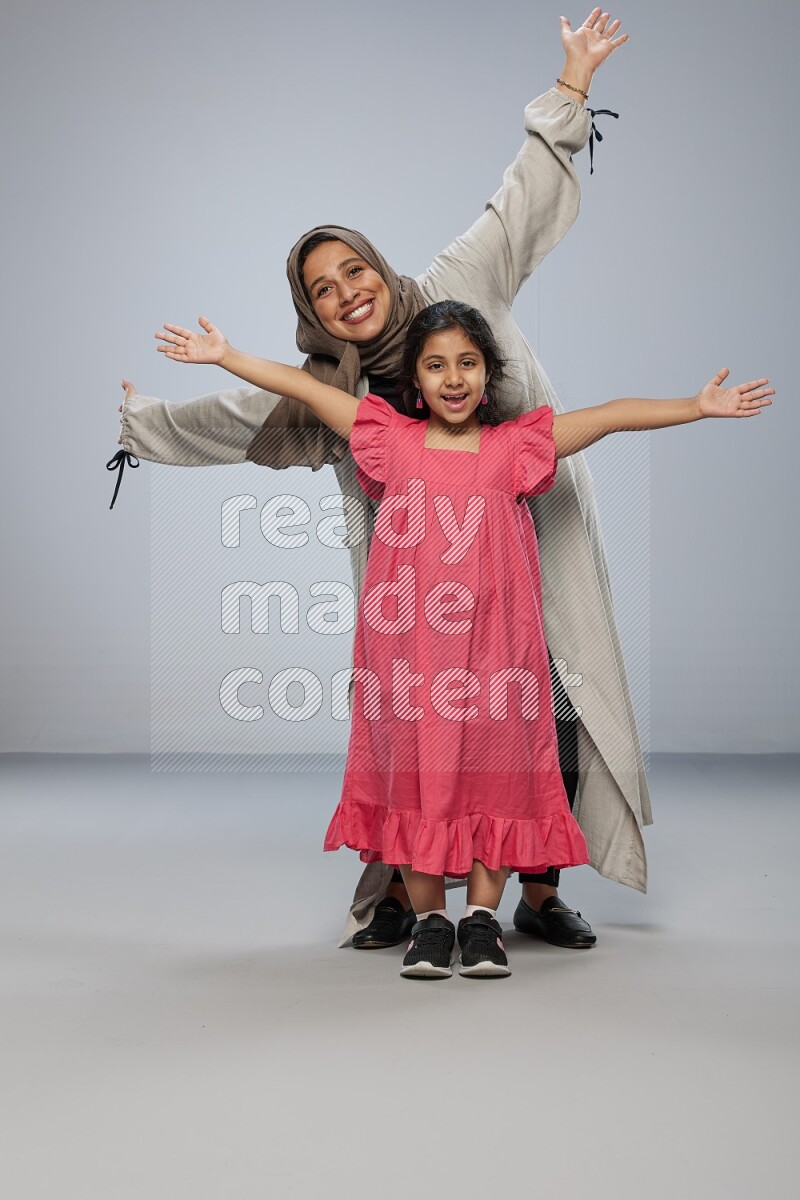 A girl and her mother interacting with the camera on gray background
