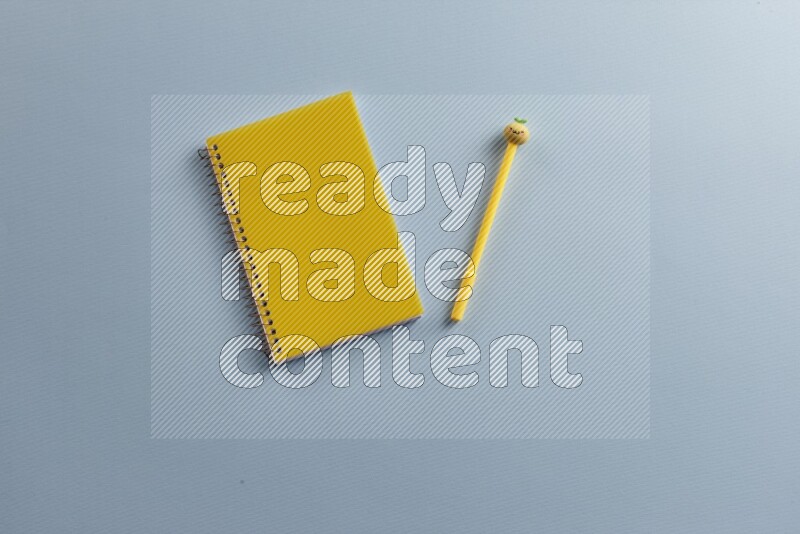 A yellow notebook with different school supplies on blue background