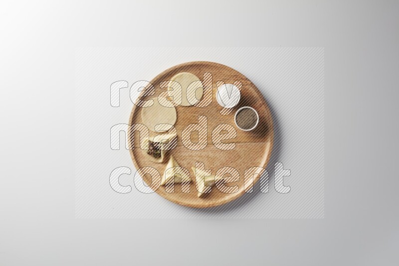 two closed sambosas and one open sambosa filled with meat while salt and black pepper aside in a wooden dish on a white background