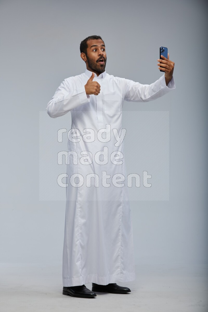 Saudi man wearing Thob standing taking selfie on Gray background