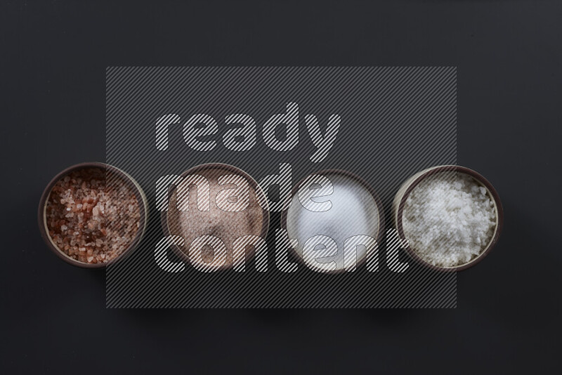 4 pottery bowls filled with himalayan salt and white salt on black background