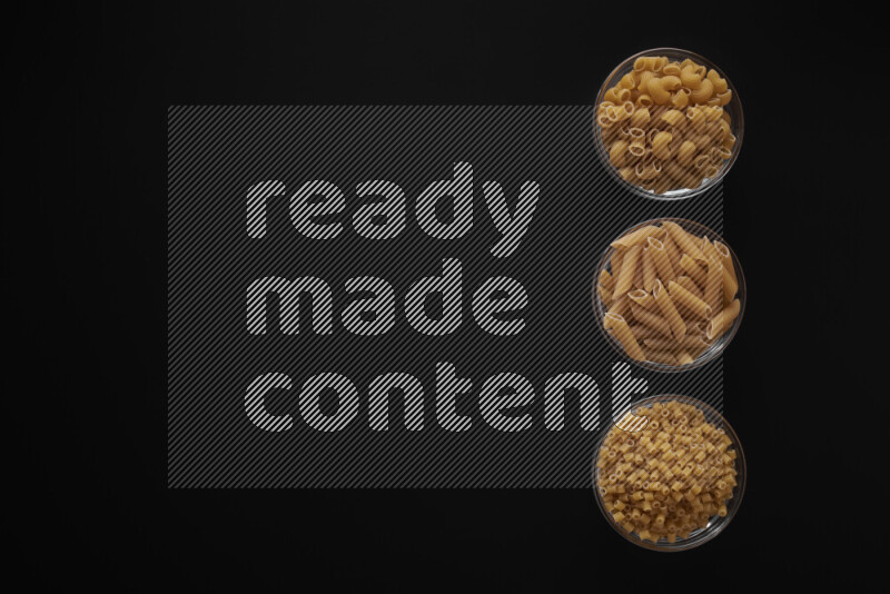 Different pasta types in 3 glass bowls on black background