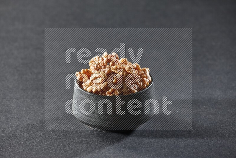 A black pottery bowl full of peeled walnuts on a black background in different angles