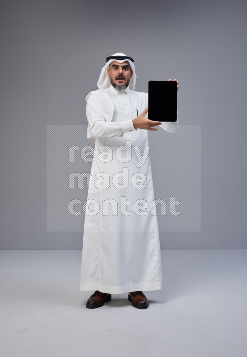 رجل سعودي يرتدي ثوب وشماغ ابيض ويحمل تابلت