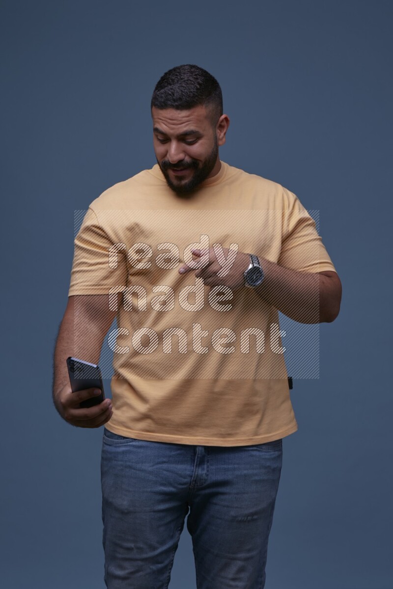 A man Pointing at a Smartphone on Blue Background wearing Orange T-shirt
