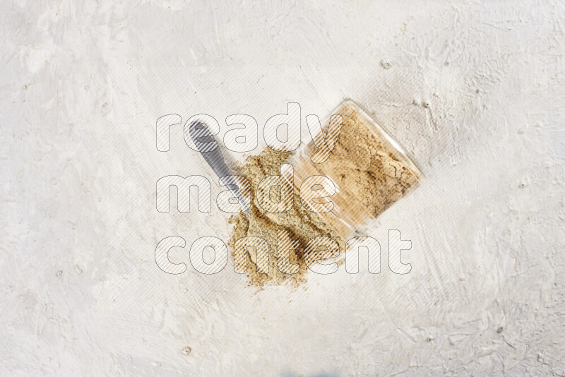 A glass jar full of ground ginger powder flipped with some spilling powder on white background