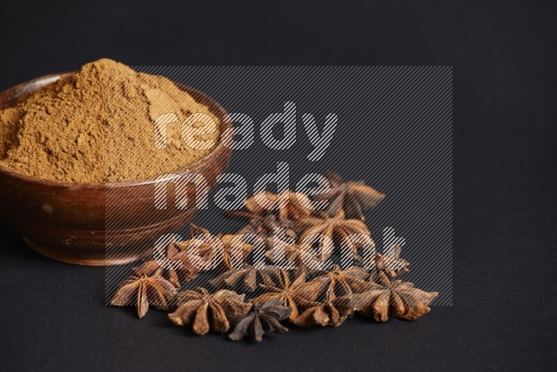 Star Anise powder in a wooden bowl with star anise beside it on a black background