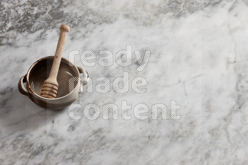 Multicolored pottery bowl with wooden honey dipper in it on grey marble background