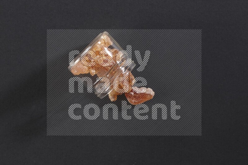 A glass jar full of gum arabic and jar is flipped and gum spread out on black flooring