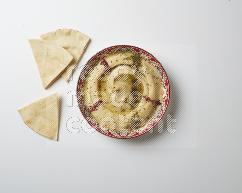 Hummus in a red plate with patterns garnished with zaatar & sumak on a white background