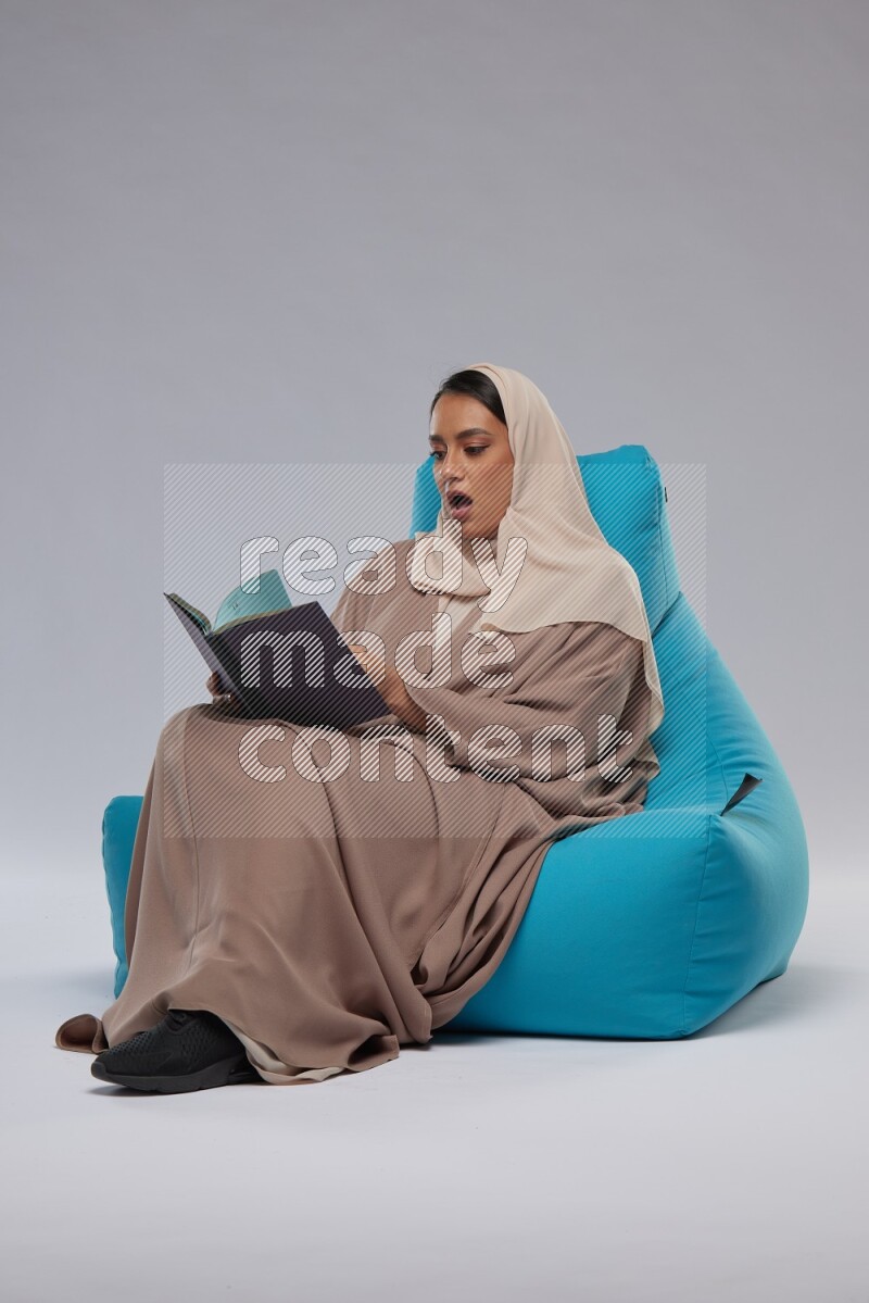 A woman sitting on a blue beanbag and reading a book