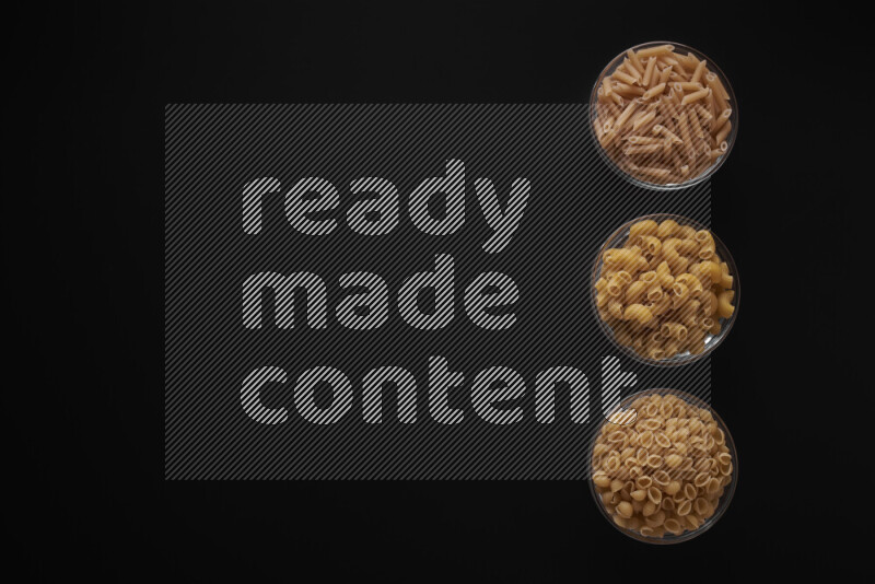 Different pasta types in 3 glass bowls on black background