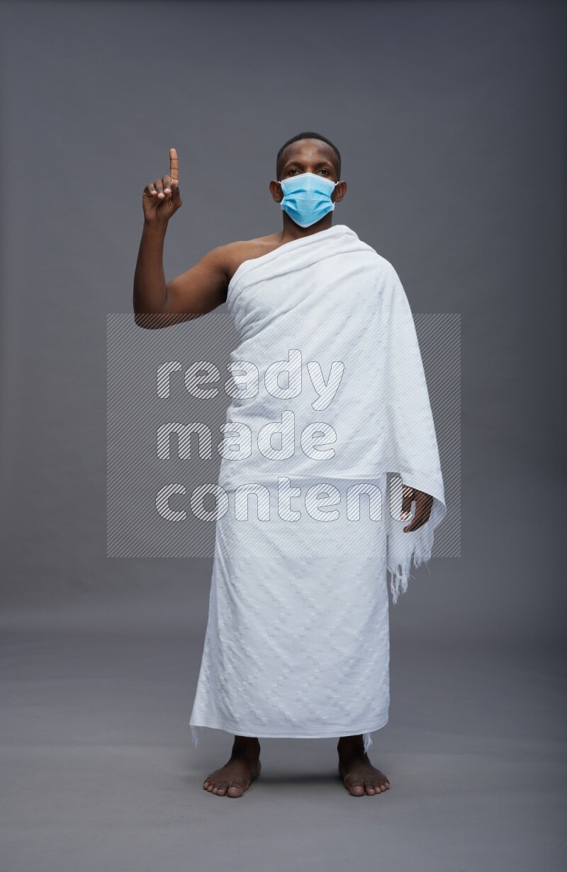 A man wearing Ehram with face mask Standing Interacting with the camera on gray background