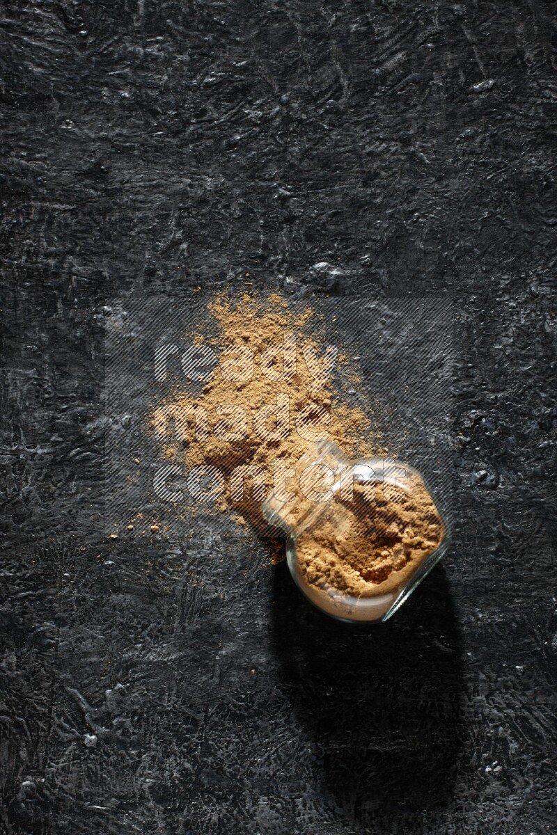 وعاء زجاجي للتوابل مقلوب ممتلئ ببودرة بهار الفلفل الحلو والبودرة تناثرت منه على خلفية سوداء