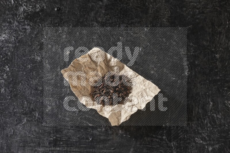 Cloves in crumpled piece of paper on a textured black flooring