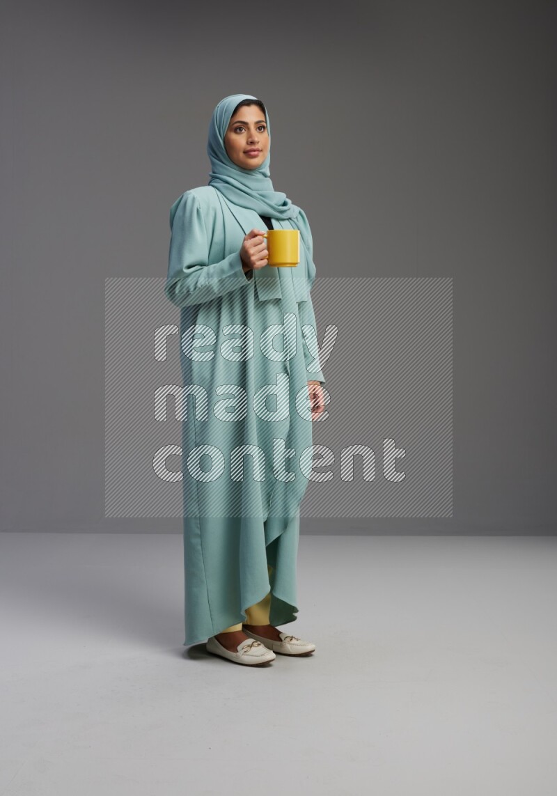 Saudi Woman wearing Abaya standing  holding a mug on Gray background