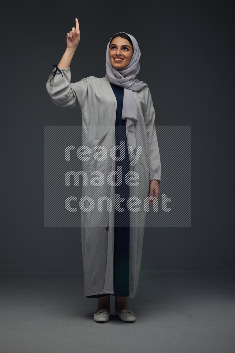 A Saudi woman wearing a light gray Abaya and head scarf standing and making multi poses eye level on a grey background