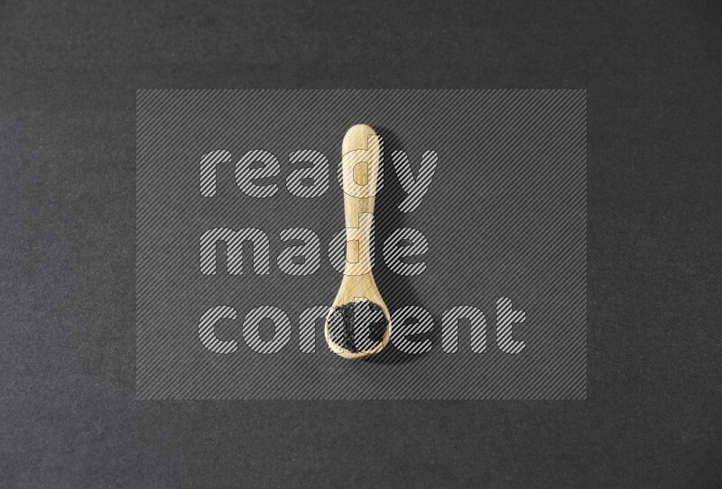 A wooden spoon full of black seeds on a black flooring