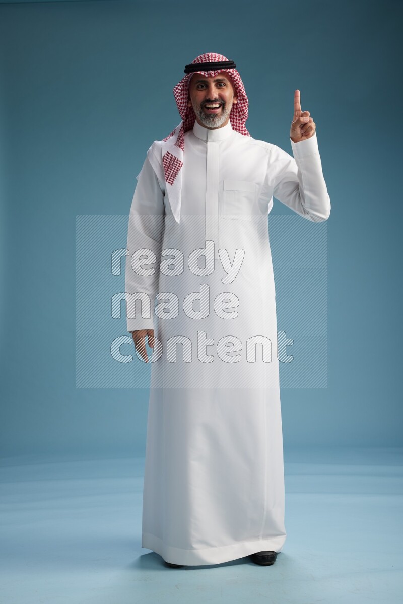 Saudi man wearing thob and shomagh posing to the camera on blue background