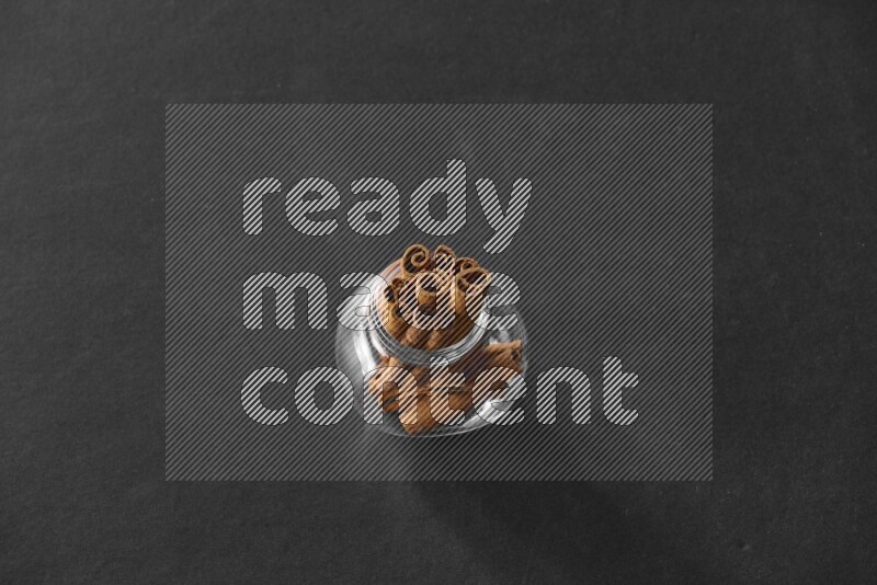 A glass spice jar full of cinnamon sticks on black flooring