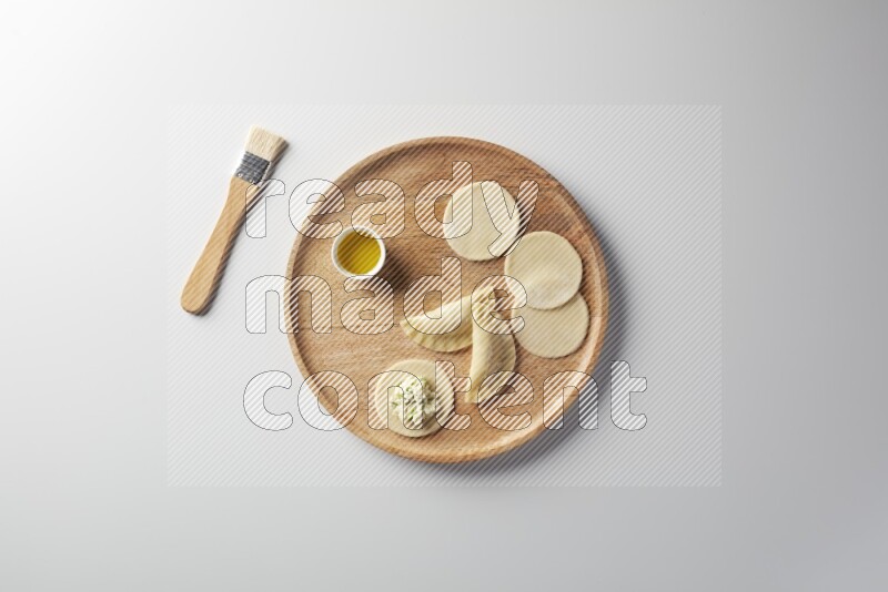 two closed sambosas and one open sambosa filled with cheese while oil with oil brush aside in a wooden dish on a white background