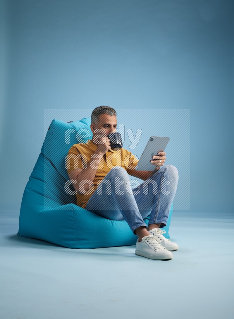 A man sitting on a blue beanbag and drinking coffee