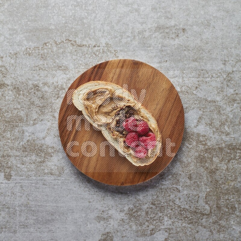 open faced peanut butter sandwich with raspberries and chocolate granula on a grey textured background