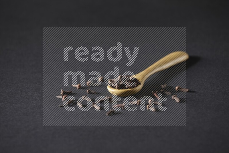 حبوب القرنفل في ملعقة خشبية وبعض من الحبوب تناثرت بخارجها علي خلفية سوداء