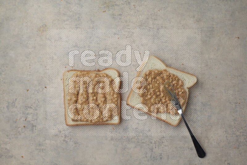 crunchy peanut butter on a white toast with a spreading knife on a light blue textured background