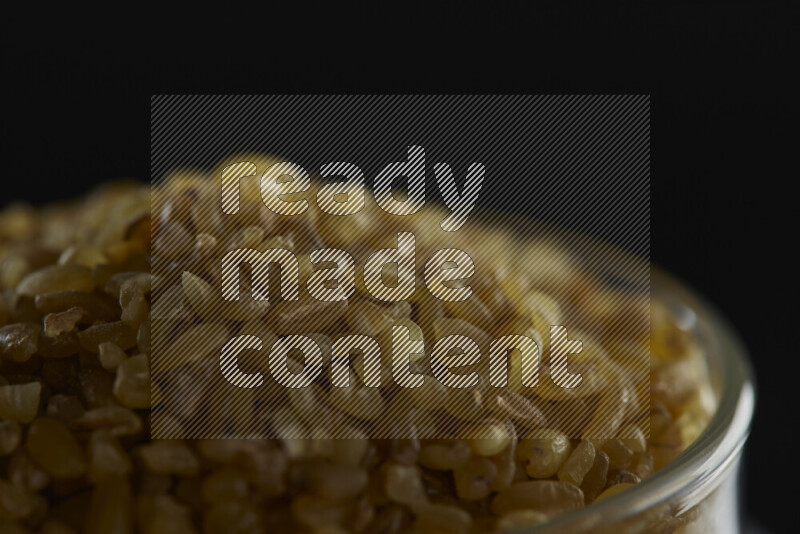 Coarse bulgur in a glass jar on black background