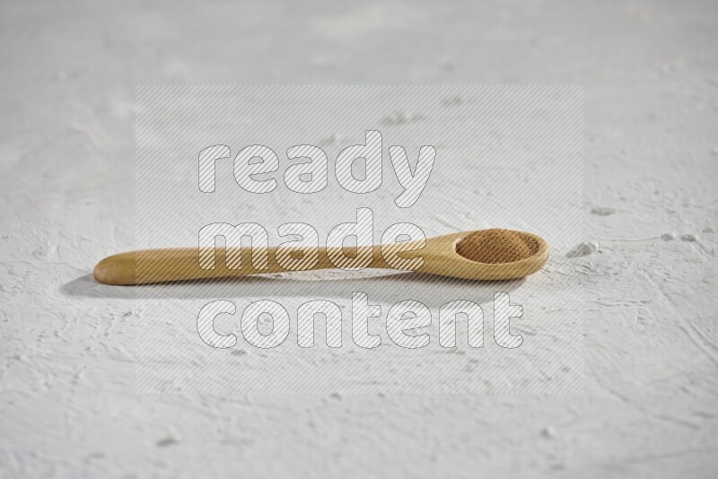 Cinnamon powder in a wooden spoon on a white background