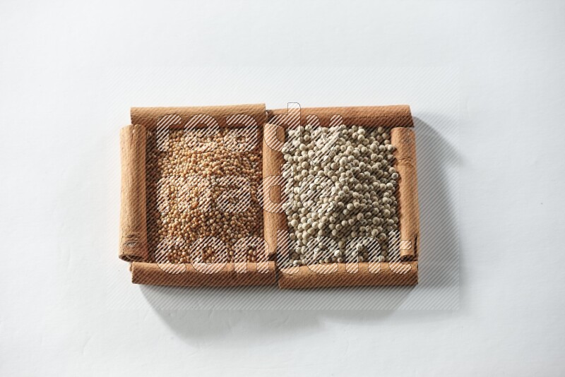 مربعان من أعواد القرفة ممتلئان بحبوب الخردل وحبوب الفلفل الأبيض علي خلفية بيضاء
