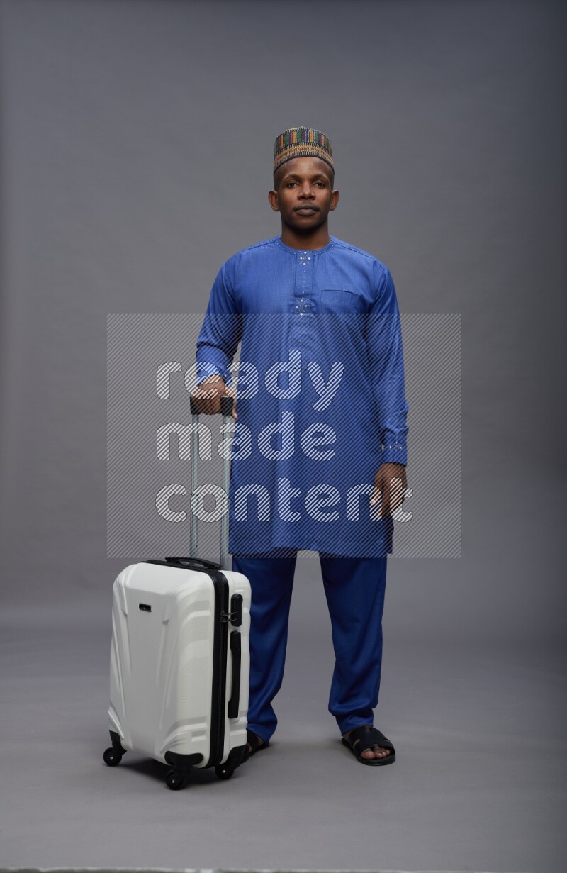 Man wearing Nigerian outfit standing holding bag on gray background