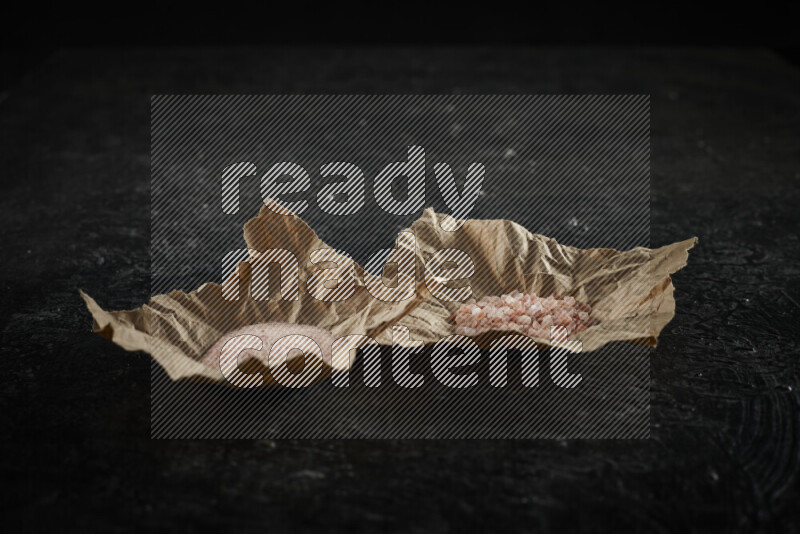 A crumpled piece of paper full of pink himalayan salt on black background