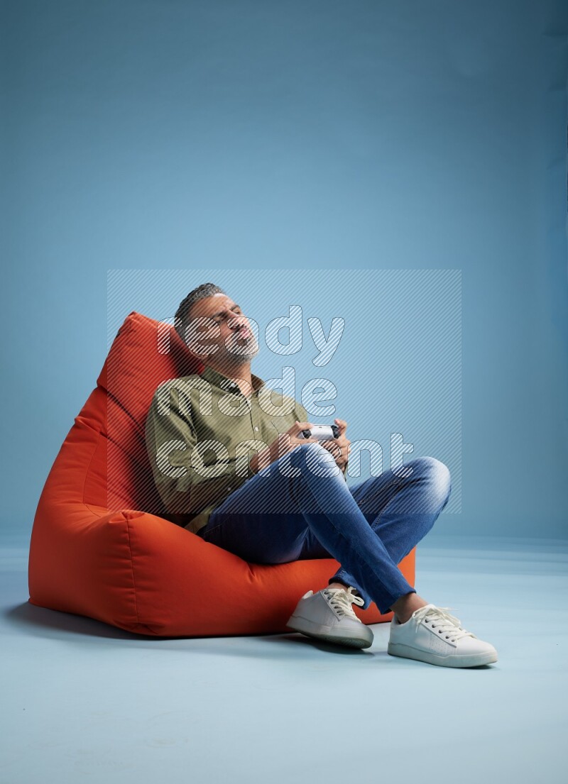 A man sitting on an orange beanbag and gaming with joystick
