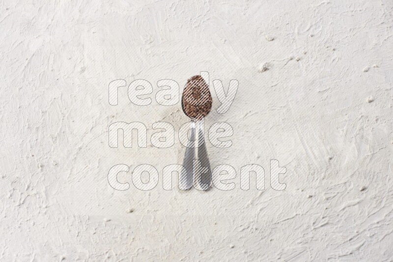 2 metal spoons full of flax seeds on a textured white flooring