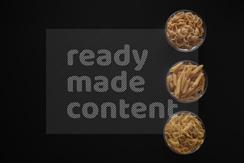 Different pasta types in 3 glass bowls on black background