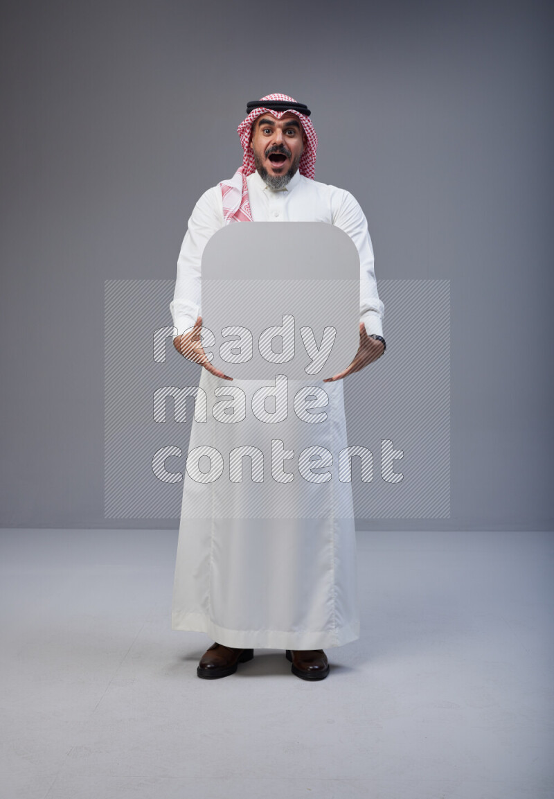 Saudi man Wearing Thob and red Shomag standing holding social media sign on Gray background