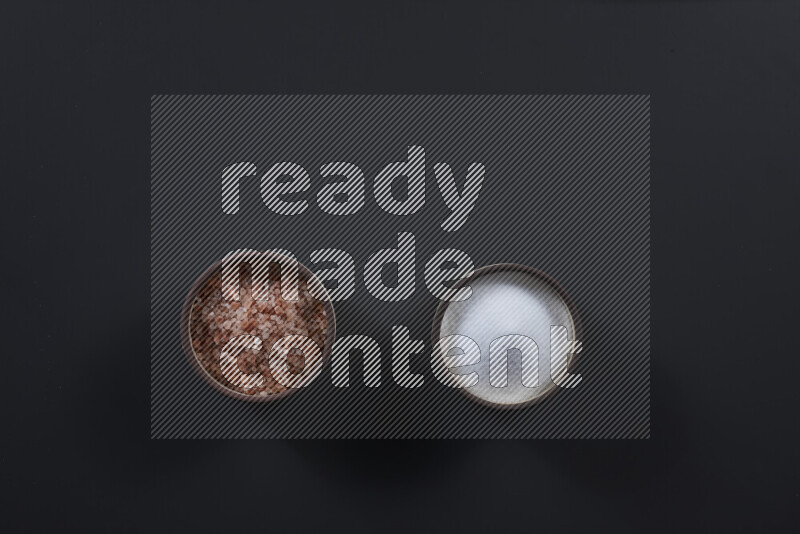 2 pottery bowls one is filled with himalayan salt and the other with white salt on black background
