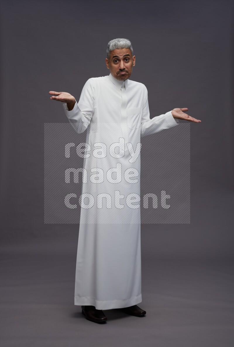 Saudi man wearing thob standing interacting with the camera on gray background