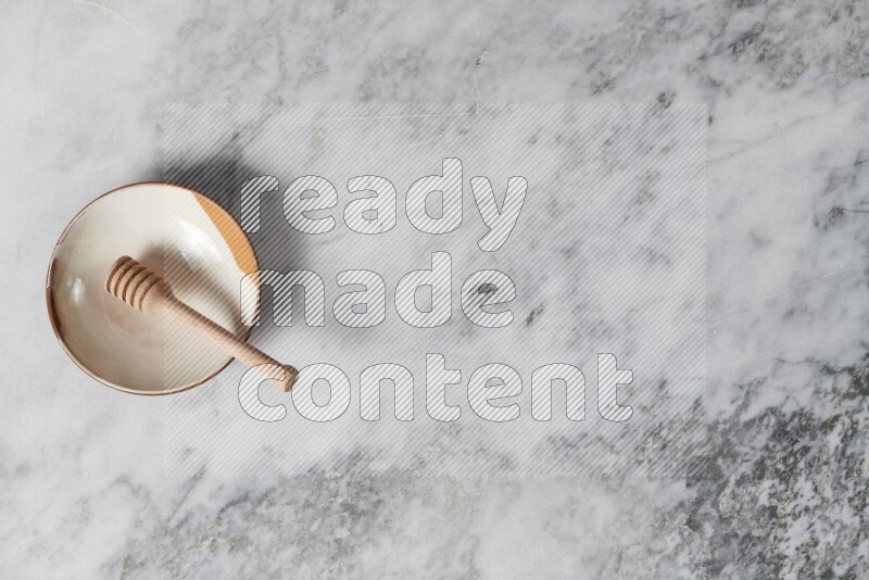 Multicolored pottery plate with wooden honey dipper in it on grey marble background