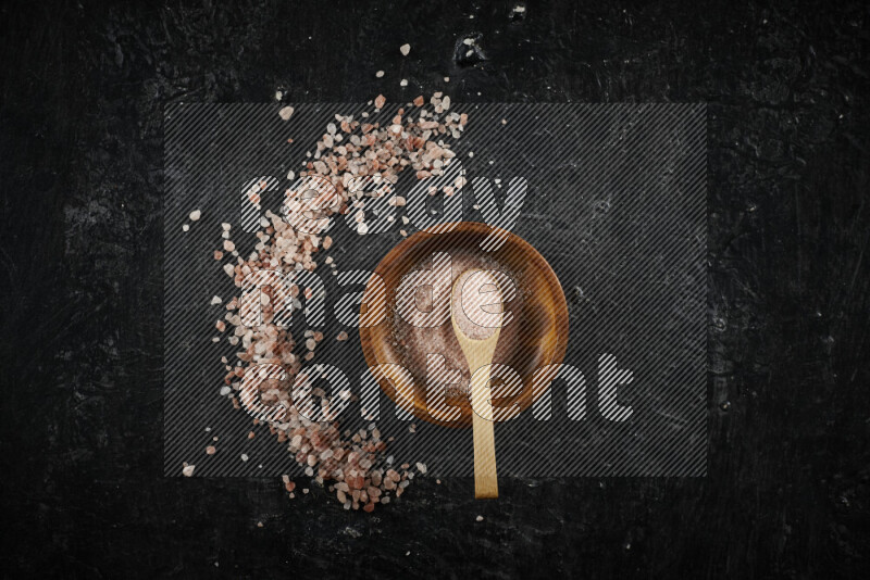 A pottery plate full of fine salt with bunch of coarse salt beside it on black background