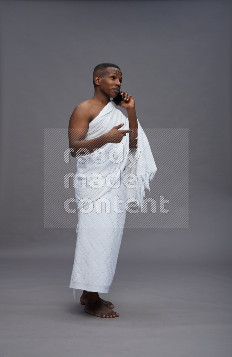 A man wearing Ehram Standing talking on phone on gray background