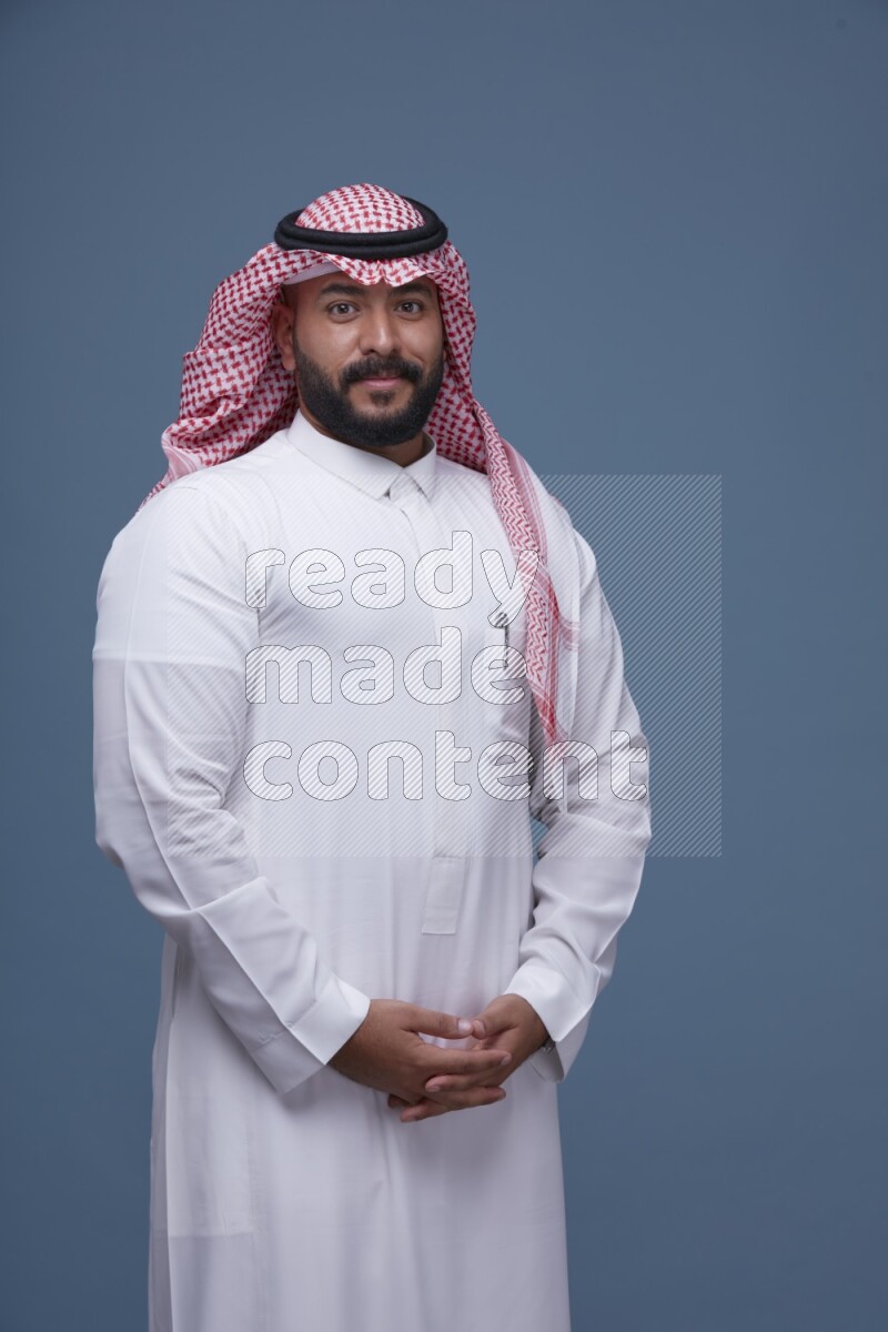 A Saudi man posing on blue background wearing Thob and Shomag
