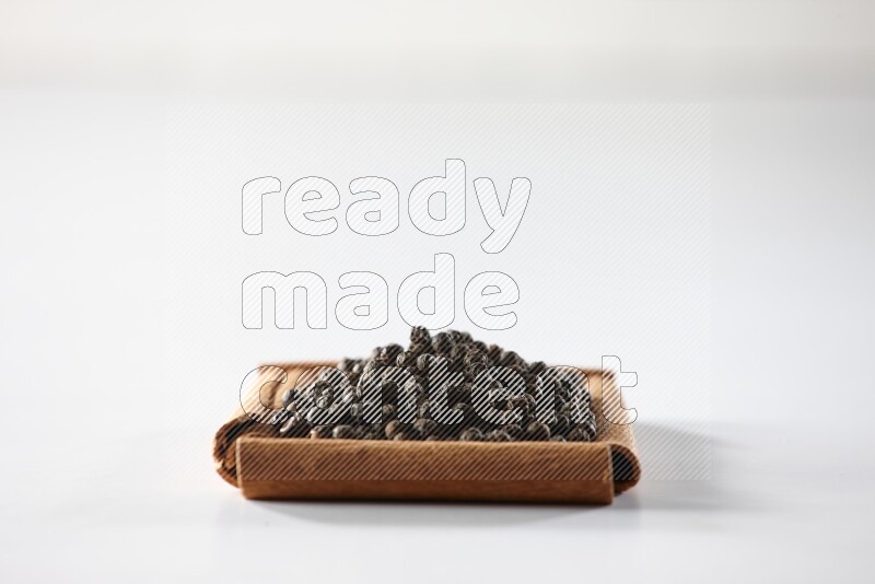A single square of cinnamon sticks full of black pepper on white flooring