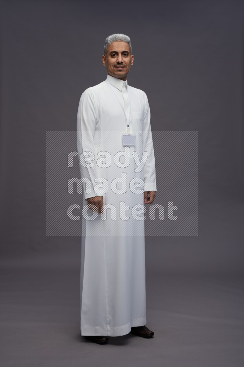 Saudi man wearing thob with neck strap employee badge standing interacting with the camera on gray background