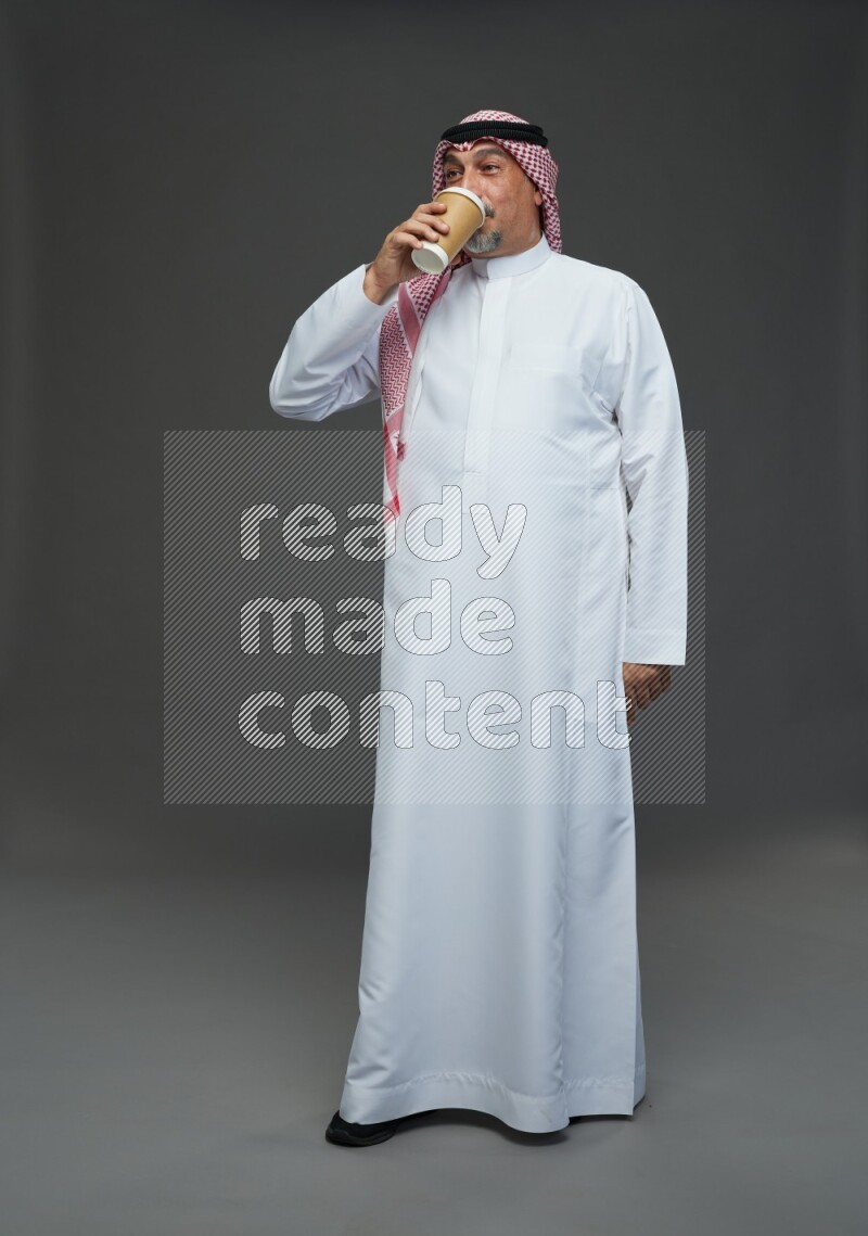 Saudi man with shomag Standing holding paper cup on gray background
