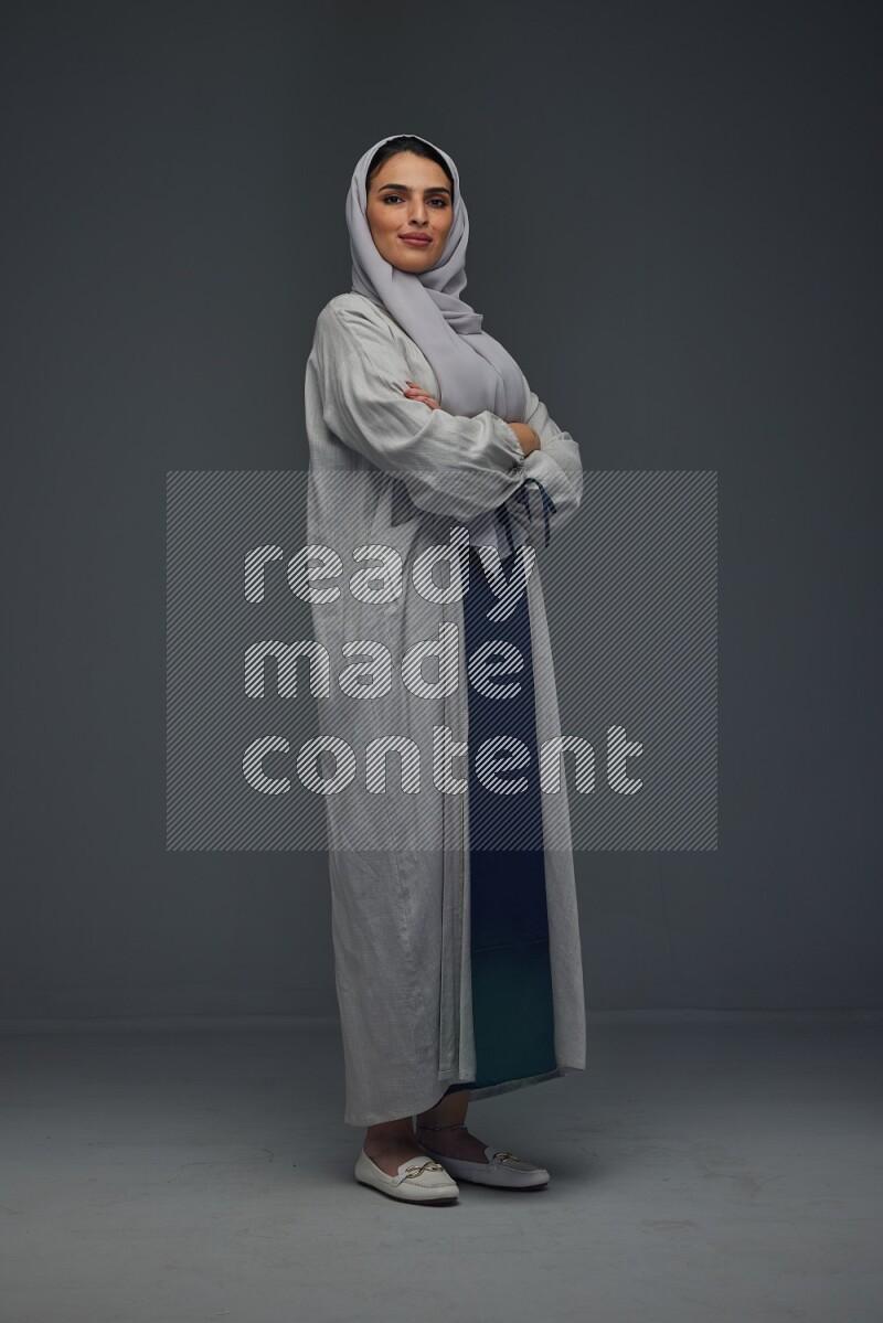 A Saudi woman wearing a light gray Abaya and head scarf standing and making multi poses eye level on a grey background
